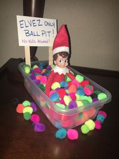 an elf is sitting in a plastic container filled with pom - poms and a sign that says elvez only ball pit