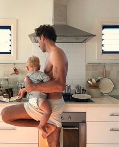 a man holding a baby while sitting on top of a kitchen counter