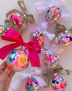 a hand holding a pink and white ornament next to other christmas ornaments with bows