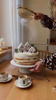 a woman is pouring frosting onto a cake on a table with cups and saucers