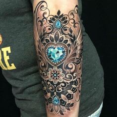 a woman with a tattoo on her arm is wearing a black and grey shirt that has blue jewels in it