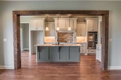 an empty kitchen with wooden floors and white cabinets in the center, surrounded by wood beams