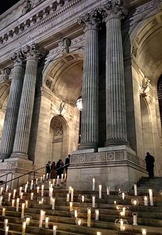 many candles are lit in front of a large building with columns and pillars on either side