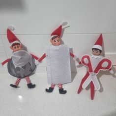 three elfs are standing next to each other on the counter with paper and scissors