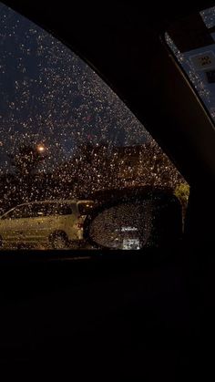 rain is falling from the sky in front of a car at night, with lights on