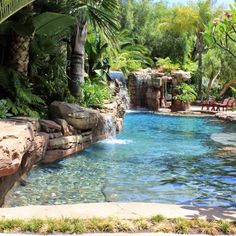 an outdoor pool surrounded by palm trees and water features a waterfall that flows into it