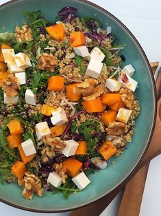 a salad with tofu, carrots and spinach in a blue bowl on a white table