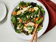 a salad with apples, cheese and spinach in a white bowl on top of a red napkin