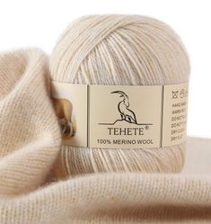 a white ball of yarn sitting on top of a pile of cloths next to a label that reads tehete 100 % merino wool