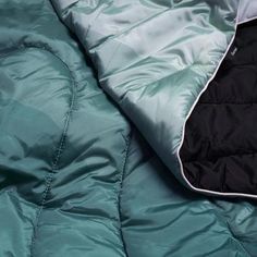 an open jacket laying on top of a green bed spread with black and white zippers