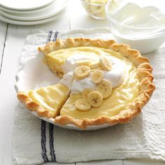 a pie with bananas and whipped cream on top is sitting on a white tablecloth