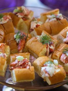 many small sandwiches on a glass plate with condiments in the middle and garnishes around them