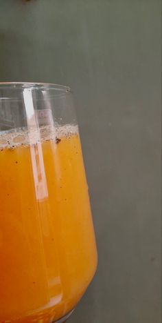 a glass filled with orange juice sitting on top of a table next to a wall