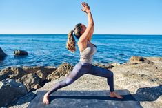 a woman doing yoga on the rocks by the ocean with her arms in the air