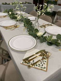 the table is set with white and gold place settings, greenery, and napkins