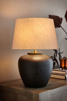 a table lamp sitting on top of a wooden table next to a book and vase