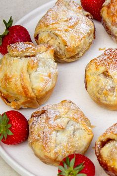 a white plate topped with pastries covered in powdered sugar next to strawberries