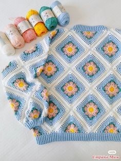 a crocheted sweater with flowers and yarns on the table next to it