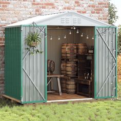 a green shed with lots of barrels in front of it and a brick wall behind it