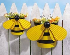 two yellow and black bee shaped planters on a white picket fence with flowers in them