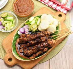 a plate with meat, vegetables and sauces on it next to a cutting board