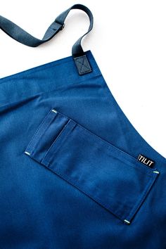 the back pocket of a blue apron on a white surface with a black strap hanging from it