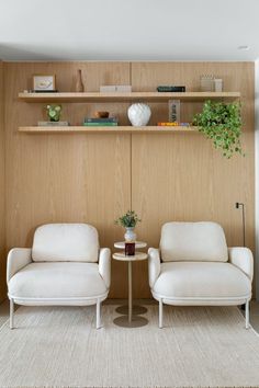 two white chairs sitting next to each other in front of a shelf with books on it