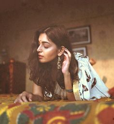 a woman laying on top of a bed next to a wooden table with a lamp