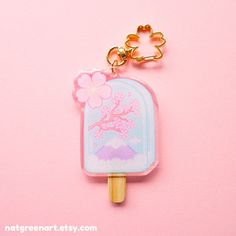 a popsicle shaped keychain with a cherry blossom on it and a pink background