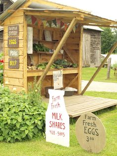 an outdoor market with fresh produce and signs on the side of it in front of a building