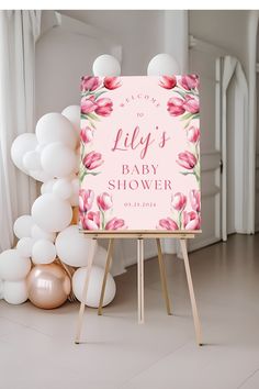 a baby shower sign with balloons in the background and a pink floral design on it