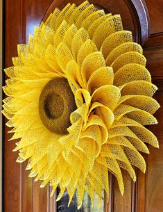 a large yellow sunflower hanging from the side of a wooden door with burlocks