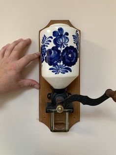 a wall mounted clock with blue and white flowers on it's face, being held by a hand