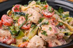 a black bowl filled with pasta covered in meat and veggies on top of a wooden table