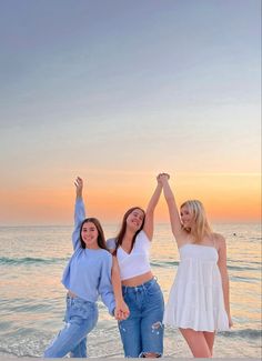 three women standing on the beach with their arms in the air