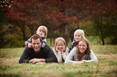 a family laying on the grass in front of some trees with their arms around each other