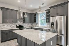 a large kitchen with gray cabinets and stainless steel appliances in the center, along with marble counter tops