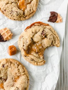 three cookies with caramel and chocolate chips on top sitting on wax paper next to a fork