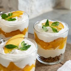 two glasses filled with ice cream, fruit and mint garnish on a table