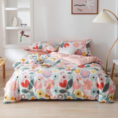 a bed with colorful flowers on it in a room next to a table and lamp