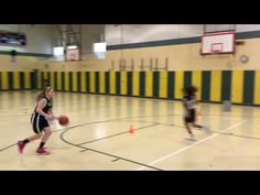 two girls playing basketball in a gym with yellow and black striped walls, one girl dribbling the ball