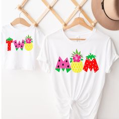 two t - shirts with pineapples and watermelon on them hanging up against a wall