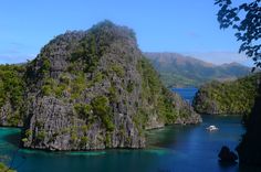 an island in the middle of some water surrounded by mountains and trees with boats on it