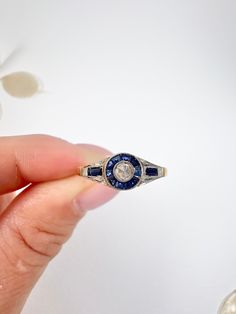 a person holding a ring with a diamond and blue sapphire in it's center