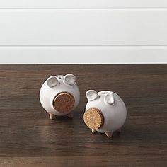 two white ceramic pig figurines sitting on top of a wooden table next to each other