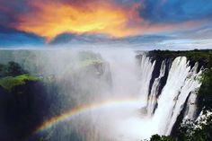 a rainbow in the sky over a waterfall with water pouring from it's side