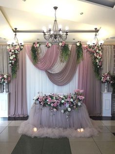 a table with flowers and candles on it in front of a curtained wall,