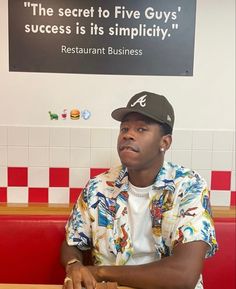 a man sitting at a table with a hot dog in his hand and a sign above him