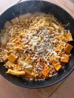 a skillet filled with pasta and cheese on top of a wooden table