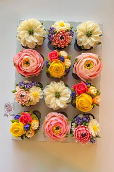 cupcakes decorated with colorful flowers are arranged in a square box on a table